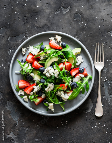 Arugula, strawberry, gorgonzola, avocado salad on a dark background, top view