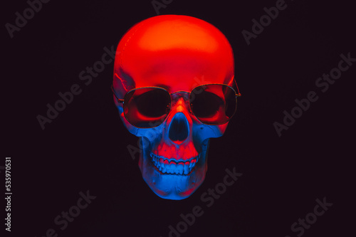 human skull wearing sunglasses in red and blue neon light on a dark background
