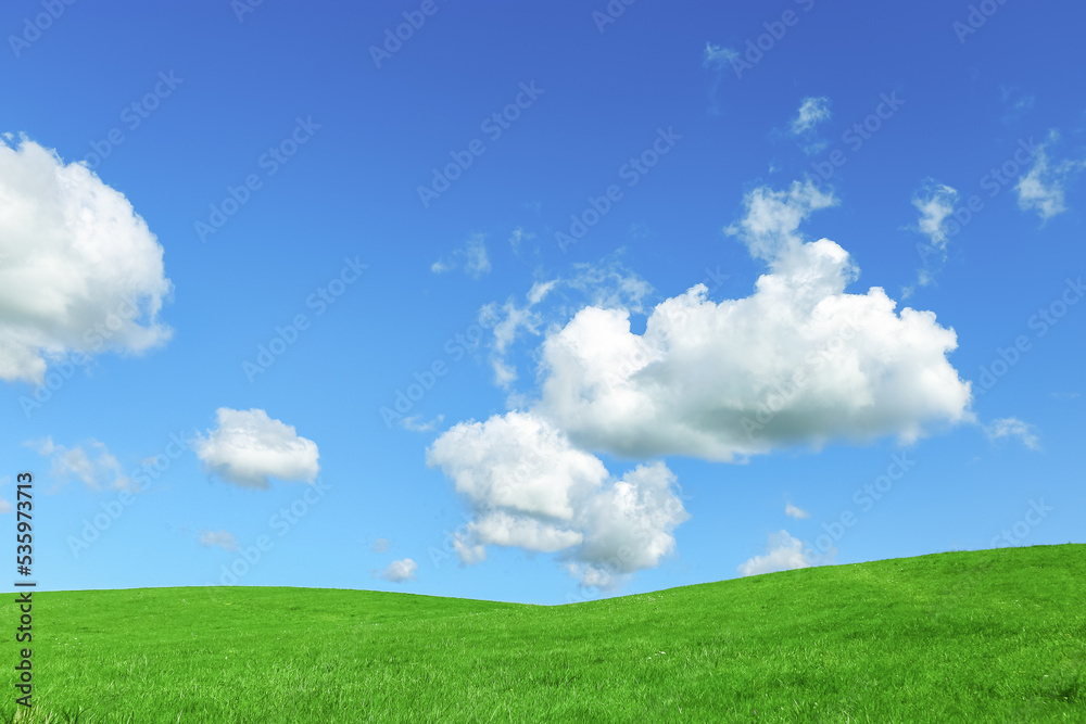 Green grass field and blue sky with clouds, aesthetic nature background. Idyllic grassland, summer or spring landscape, green countryside fields, blue sky cloudy, bright environmental nature