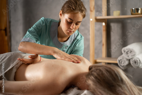 masseur massaging shoulder of young woman. Female patient getting remedial body and shoulder blade massage easing pain and relaxing muscles. photo