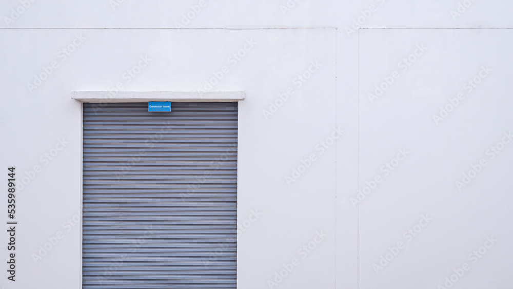 Roller shutter door of generator room on white concrete wall, front view with copy space Roller shutter door of generator room on white concrete wall, front view with copy space