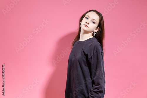 Portrait of Serious Blond Teenager girl in hoodie attentively looking at camera While posing with tilted head in studio Isolated on Pink Background