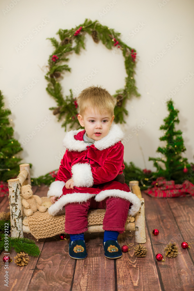 Little cute boy dressed as Santa Claus in a room decorated for Christmas. Christmas and children