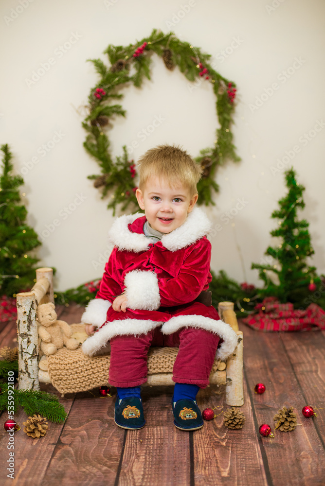 Little cute boy dressed as Santa Claus in a room decorated for Christmas. Christmas and children