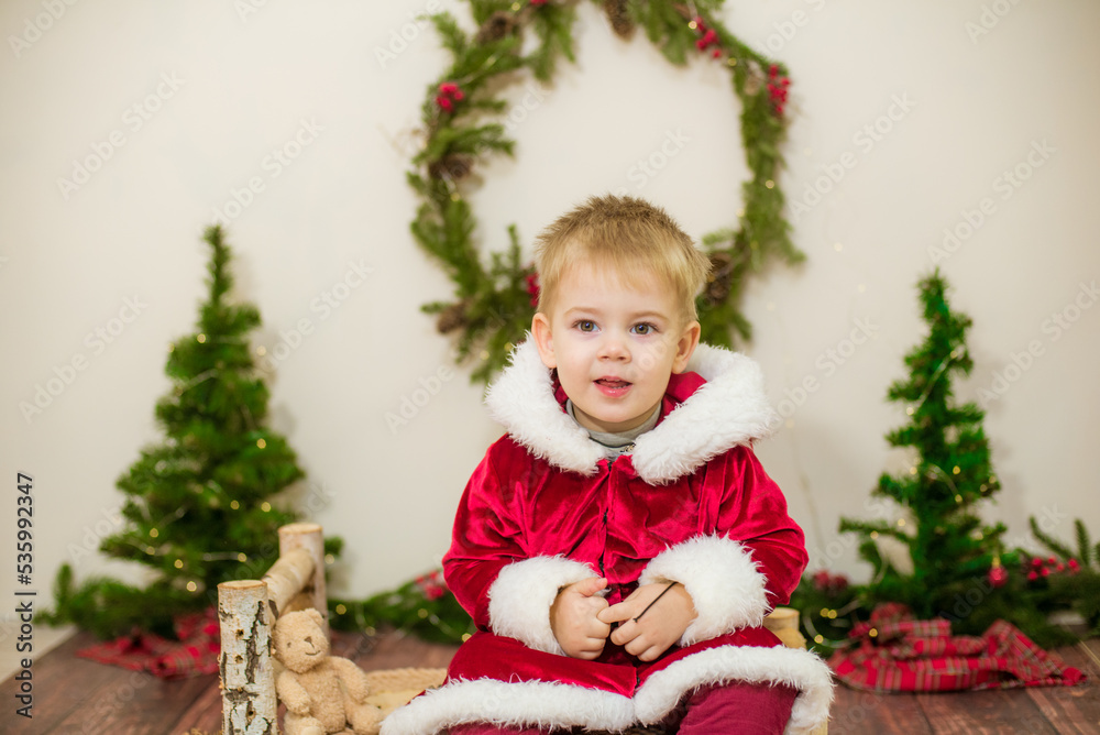 Little cute boy dressed as Santa Claus in a room decorated for Christmas. Christmas and children