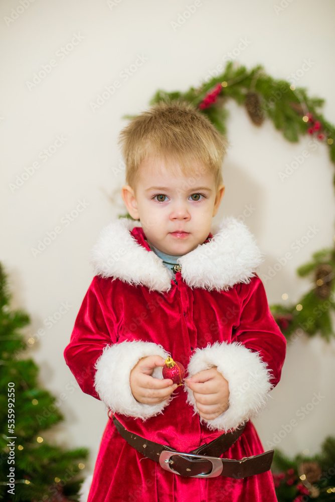 Little cute boy dressed as Santa Claus in a room decorated for Christmas. Christmas and children