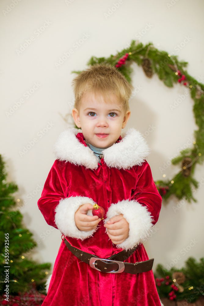 Little cute boy dressed as Santa Claus in a room decorated for Christmas. Christmas and children
