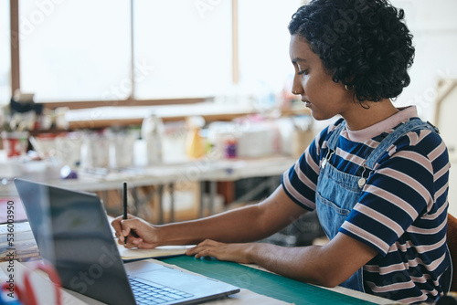 Laptop, art and education with a woman student in a creative classroom, workshop or studio while writing in a notebook. Computer, learning and school with a female artwork pupil studying in class