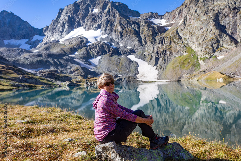 The girl sits against the backdrop of mountain peaks and a blue lake. Beautiful mountain landscape for vacation, travel and healthy lifestyle