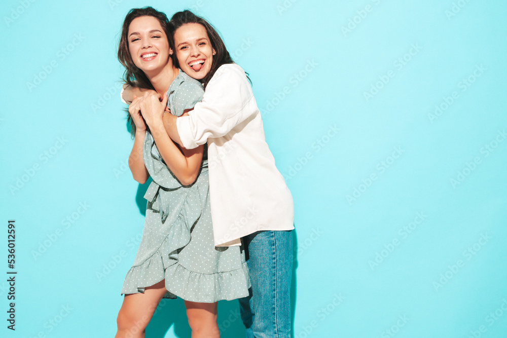 Two young beautiful smiling brunette hipster female in trendy summer shorts clothes. carefree women posing near blue wall. Positive models having fun. Cheerful and happy Two young beautiful smiling brunette hipster female in trendy summer shorts clothes. carefree women posing near blue wall. Positive models having fun. Cheerful and happy