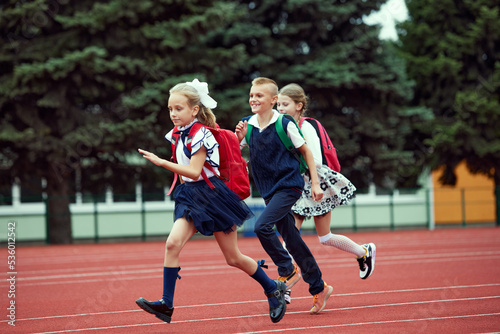 Start. Back to school, kids and education concept. Girls and boy dressed in school uniform as elementary student carrying big backpack running on treadmill at the stadium or arena.