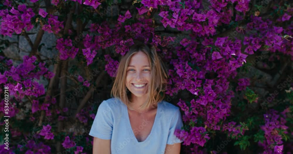 Handheld zoom out shot of authentic happy and laughing young woman with bright natural smile. Attractive and cute full of emotion and happiness woman in flowers and colors