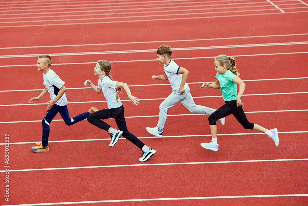 Group of children running on treadmill at stadium or arena. Little fit boys and girls in sportswear training as athletes outdoor. Concept of sport, fitness, achievements, studying, goals, skills