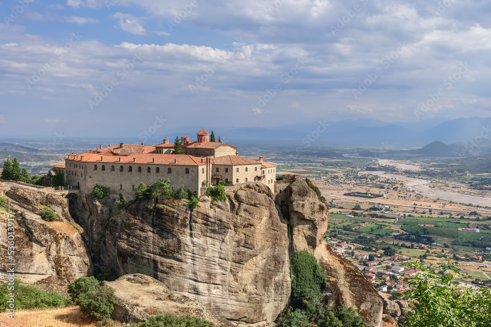 View of Thessaly valley with Kalabaka townr and historic Eastern Orthodox St. Stephen Holy Monastery nestled on a rocky plateau, Meteora, Greece.