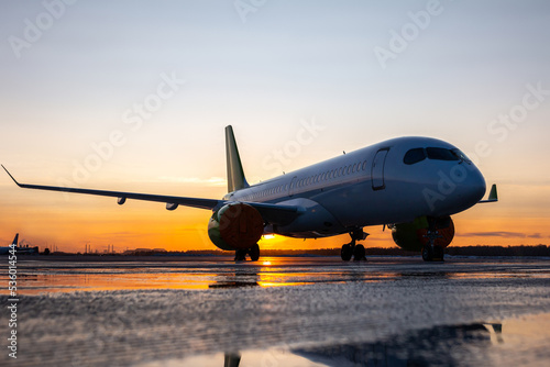 Modern passenger jetliner on the airport apron against the backdrop of a picturesque sunset with reflection in a puddle