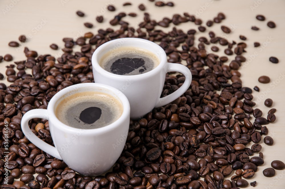 Roasted coffee espresso beans on dark background and two cups with crema, close-up, flat lay background still life hot beverage, I love coffee concept Roasted coffee espresso beans on dark background and two cups with crema, close-up, flat lay background still life hot beverage, I love coffee concept