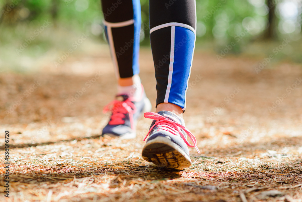 Female runner jogging forward outdoors through a summer forest trail.Close up.Copy space.