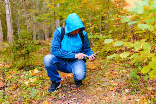 Man hiker got lost in a autumn forest and catches a mobile network on a phone.Tourist looking for a cellular connection on a hike.Travel Technology concept. © ARVD73