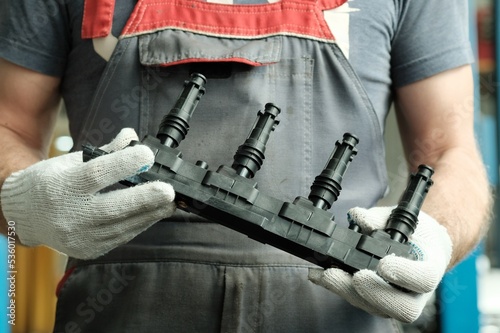 An auto mechanic holds a new induction ignition coil in his hands. Inspection and control of the integrity and compliance of a new spare part before replacement during repair at a service station.