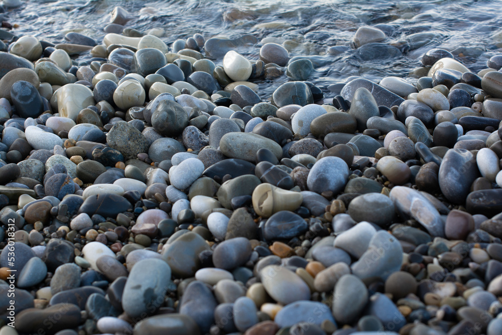 The seashore with lots of pebbles. The sea is on the horizon. A sunny morning day. Background with round stones. The stones on the beach are smooth. View from above. The seashore with lots of pebbles. The sea is on the horizon. A sunny morning day. Background with round stones. The stones on the beach are smooth. View from above.