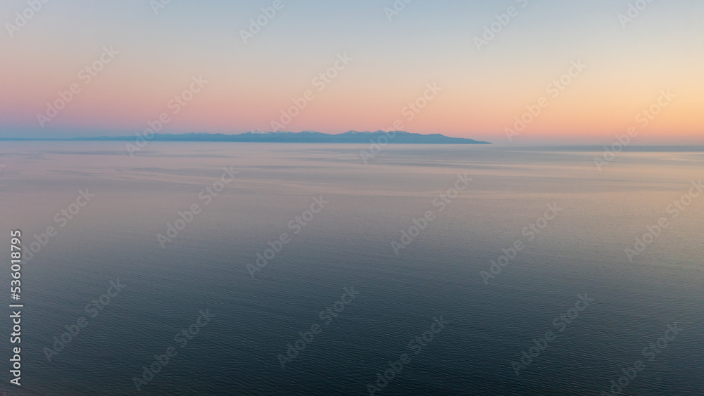 Sunset seascape. Aerial view of the sea. Mountains in the distance. Ripples on the surface of the water. Beautiful natural background. Perfect for design.