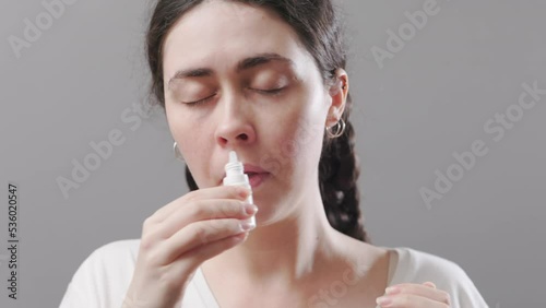 Portrait of a young woman burying drops in her nose. Treatment of runny nose and viral infections. Concept of allergy and covid-19.