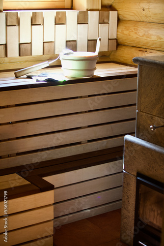 Cozy wooden interior of wood burning sauna and sauna accessories close-up. A wooden bucket, felt mitten, ladle and bamboo broom on a wooden bench. Closeup of sauna accessories in the sunshine. SPA.