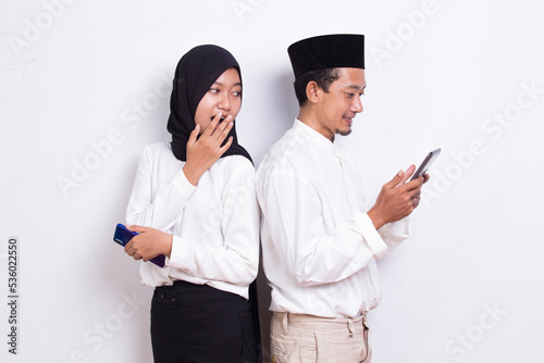Fotografie young asian muslim couple spying and peeking at smartphone isolated on white bac