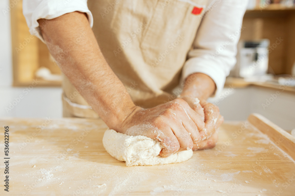 Man's hands kneading homemade dough with wheat flour close-up shot on wooden surface in modern kitchen.