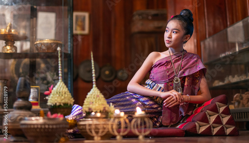 Portrait photo of a young beautiful asian Laos lady wearing traditional Lao costume dresses with flower bouquet and candles prepared for Loy Krathong festival sitting on the floor with a elegant pose