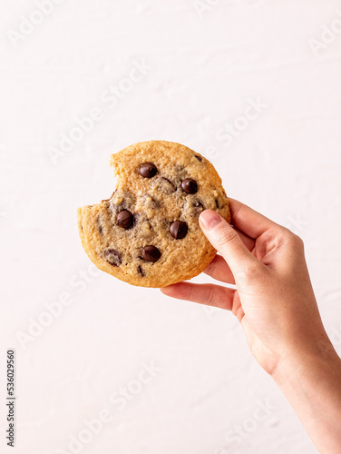 Female hand holding bitten an American chocolate chip cookie in the air in front of the white background, homemade