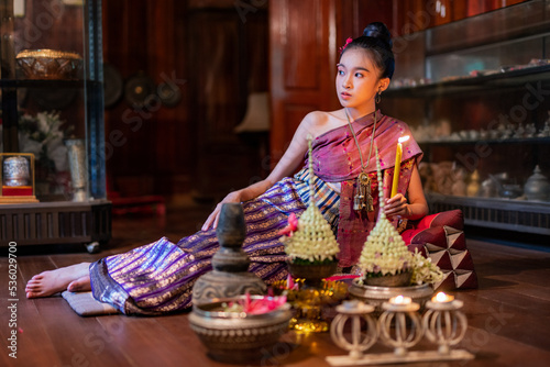 Portrait photo of a young beautiful asian Laos lady wearing traditional Lao costume dresses with flower bouquet and candles prepared for Loy Krathong festival sitting on the floor with a elegant pose