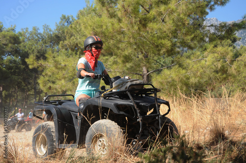 Photo of a girl on a quad bike in a helmet, ammunition. Beautiful landscape, mountain background. FeMale driver riding buggy at savannah and rough terrain, safari extreme fun. face not visible.