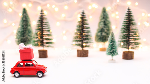 Litle red car with red gift on the roof. Creative and cute Chrsitmas background with christmas trees