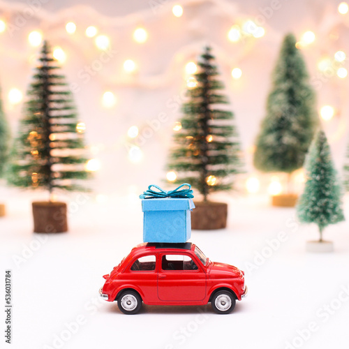 Litle red car with blue gift on the roof. Creative and cute Chrsitmas background with christmas trees