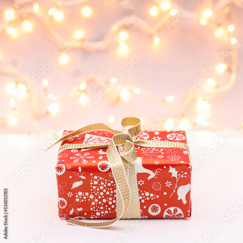 Red Christmas gift with golden ribbon with lights on background. New year concept