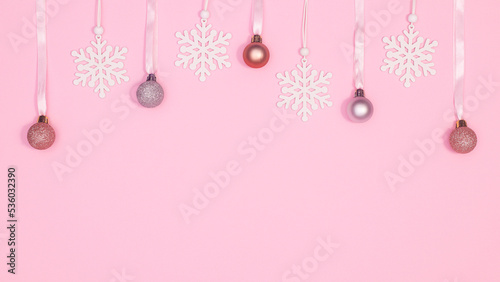 Hanging Christmas ornaments and snowflakes on pastel pink background with copy space