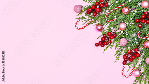 Pastel pink background with copy space and pine branches decorated with red berries and pink ornaments. Flat lay