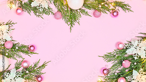 Pastel pink background with copy space and pine branches decorated with white flowers and pink ornaments. Flat lay