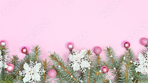 Chrsitmas garland with pine branches decorated with white flowers and pink ornaments on pastel pink copy space background. Flat lay