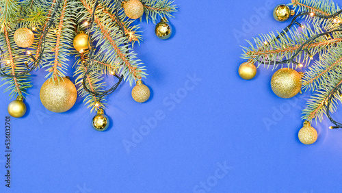 GOlden ornaments on fir branches with decorative lights on blue background. Flat lay