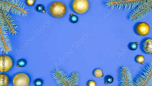 Christmas frame with vibrant blue and gold ornaments and fir branches on blue background. Glamour flat lay copy space concept