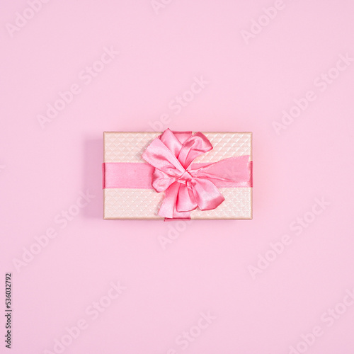 Pastel pink gift with ribbon on bright pink background. Monocgrome holidays concept