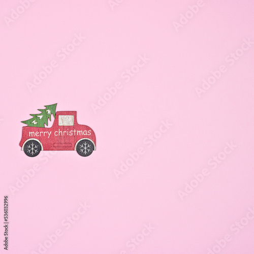 Wooden diy red car with Chrismtas tree on pastel pink background. Flat lay