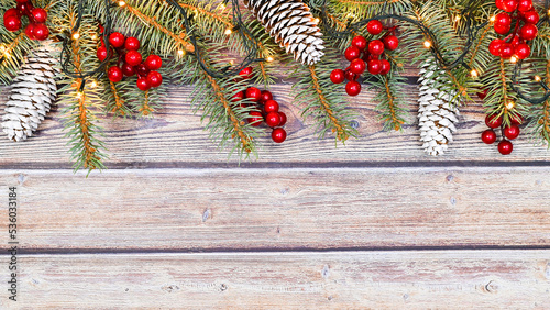 Wooden background with fir garland and red berries and pine cones. Copy space flat lay