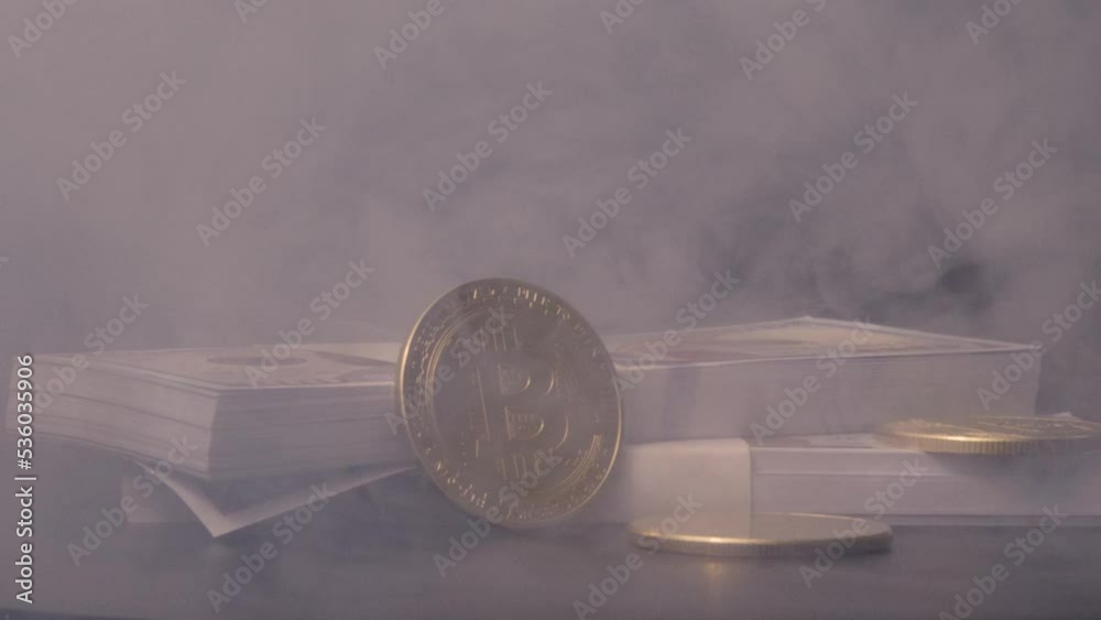 Gold Bitcoins and hundred dollar bills being revealed through smoke against black background. Gold Bitcoins and hundred dollar bills being revealed through smoke against black background.