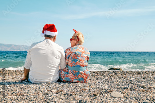 Rear view of funny adult couple wearing christmas costumes drinking sparkling wine and enjoying christmas vacations on tropical beach. Winter holiday concept.
