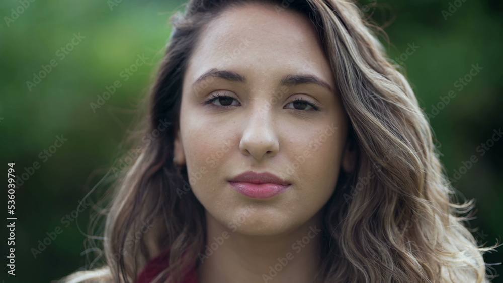 Portrait of a young hispanic woman looking at camera. Casual South American latina girl face closeup standing outdoors at park 2 Portrait of a young hispanic woman looking at camera. Casual South American latina girl face closeup standing outdoors at park 2