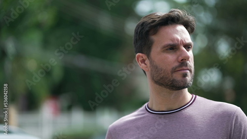 One thoughtful young man walking outdoors in city street. Pensive male 30s person walks with serious expression