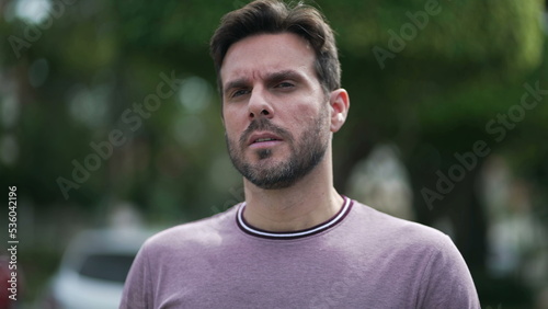 One thoughtful young man walking outdoors in city street. Pensive male 30s person walks with serious expression